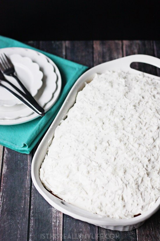 Coconut Poke Cake -- This coconut poke cake features a yellow cake infused with sweet coconut cream and topped with homemade whipped cream frosting and shredded coconut.