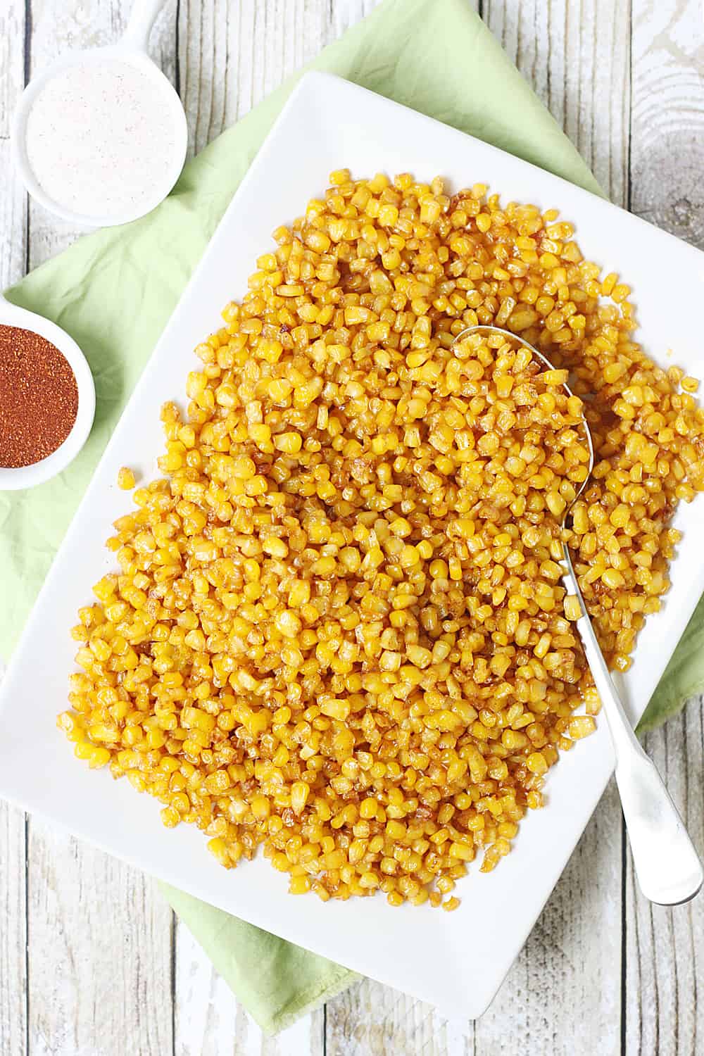 Roasted corn on a plate with a spoon.