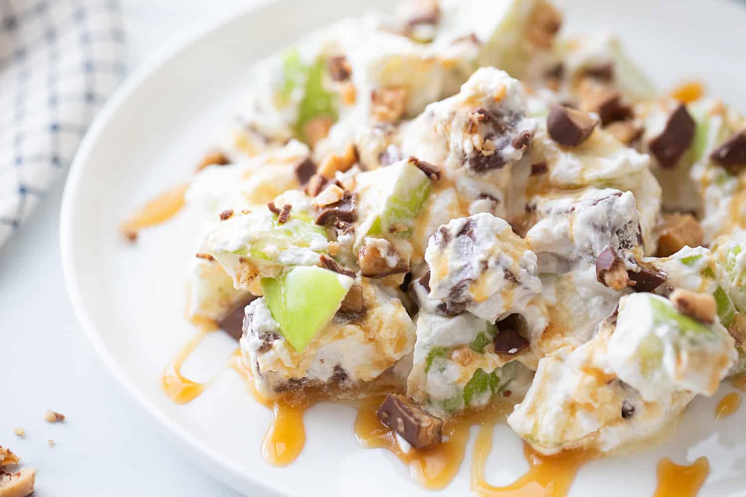 Easy Snickers Salad - This easy Snickers salad features Granny Smith apples, Snickers, and whipped topping with a drizzle of caramel and a sprinkle of toffee bits. #snickers #salad #dessert #halfscratched #easyrecipe #dessertsalad #sweets