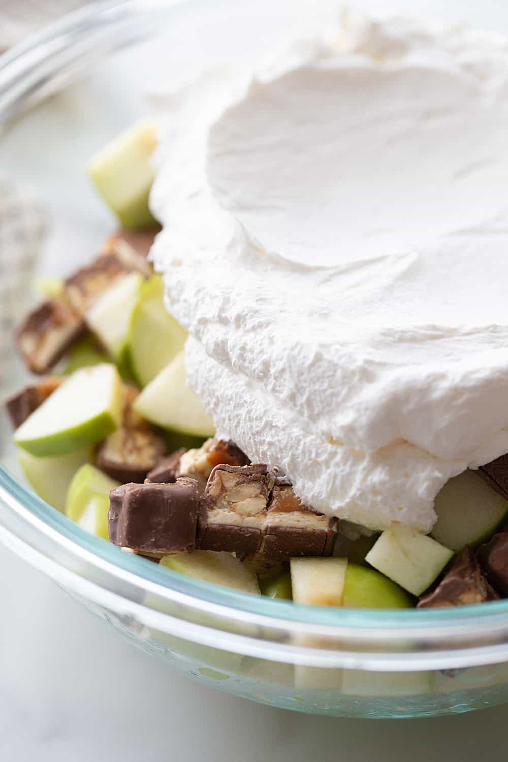 Easy Snickers Salad - This easy Snickers salad features Granny Smith apples, Snickers, and whipped topping with a drizzle of caramel and a sprinkle of toffee bits. #snickers #salad #dessert #halfscratched #easyrecipe #dessertsalad #sweets