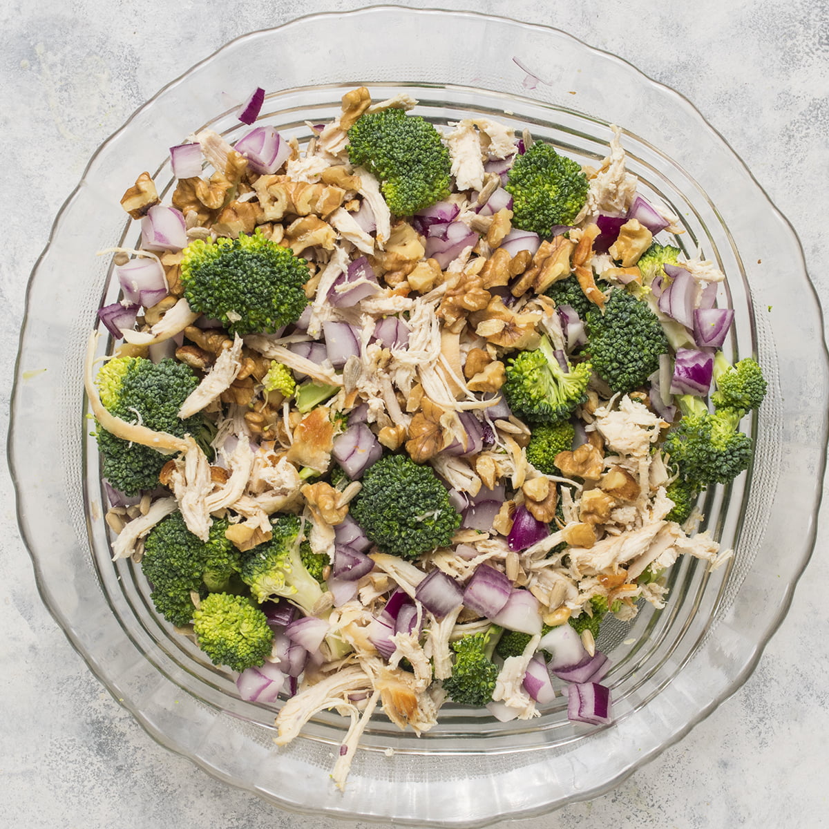 Chicken with the broccoli, sunflower seeds, walnuts, and onions in a large bowl.