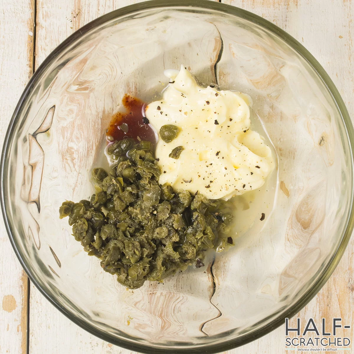 A bowl, with mayonnaise, lemon juice, capers, hot sauce, salt, and pepper.