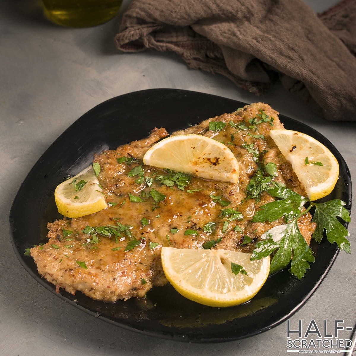 A black plate with lemon chicken piccata