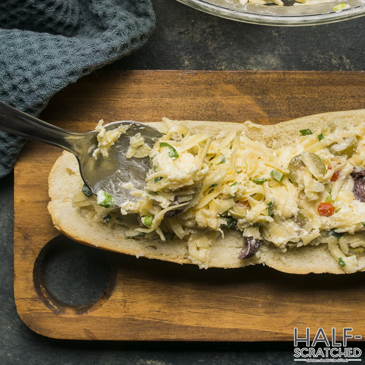 French bread being filled with olive and cheese mixture